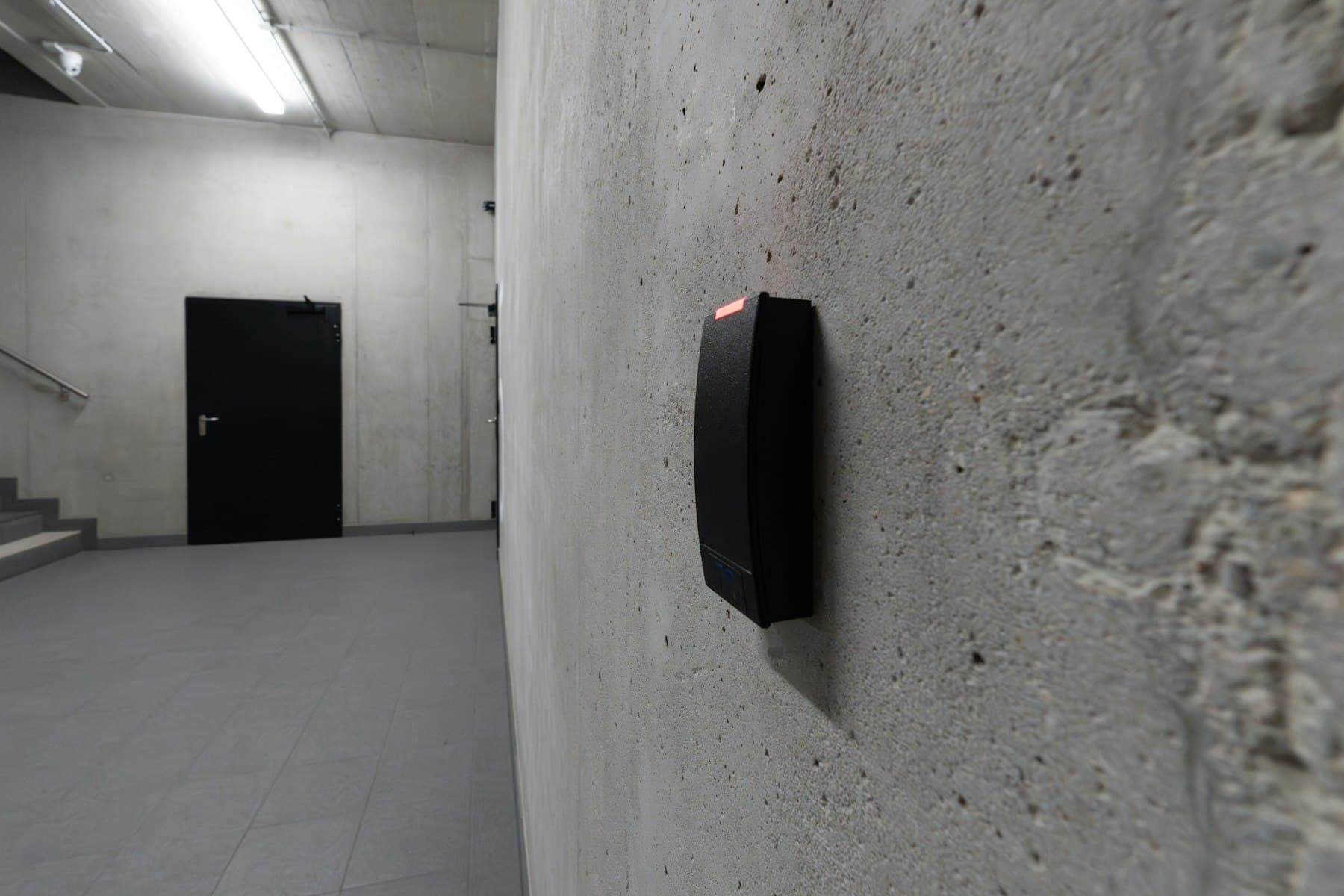 Electronic access card reader on a concrete wall beside a closed door — a physical least-privilege checkpoint
